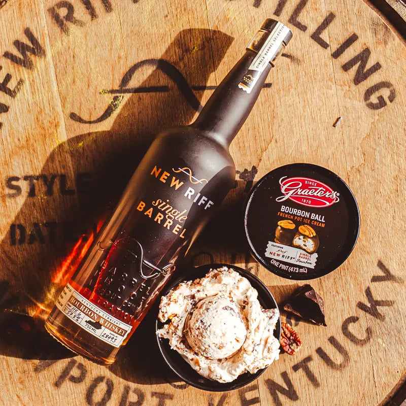 brown ice cream with chunks of pecan sitting next to a bottle of New Riff bourbon and the Graeter's Bourbon Ball ice cream on top of a barrel of bourbon