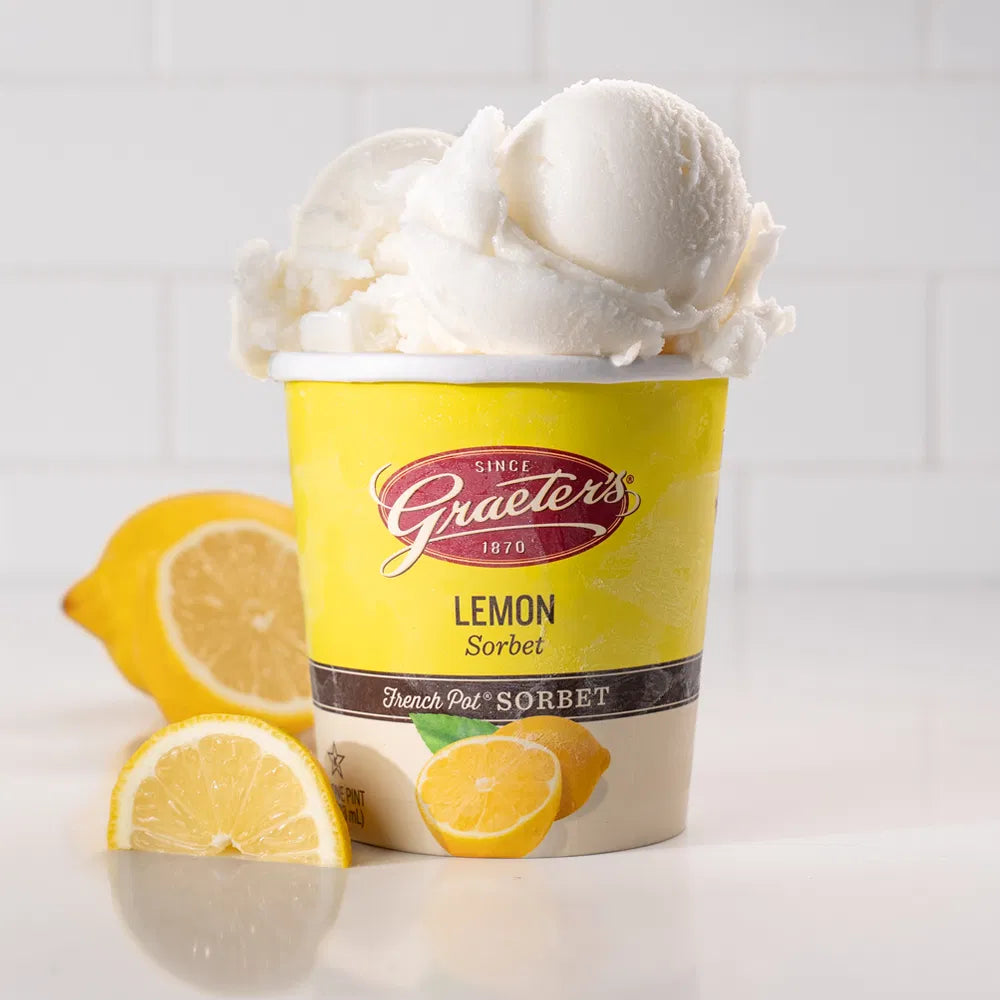 Graeter's lemon sorbet pint overflowing with pure white sorbet with lemons nestled next to it in front of a white background