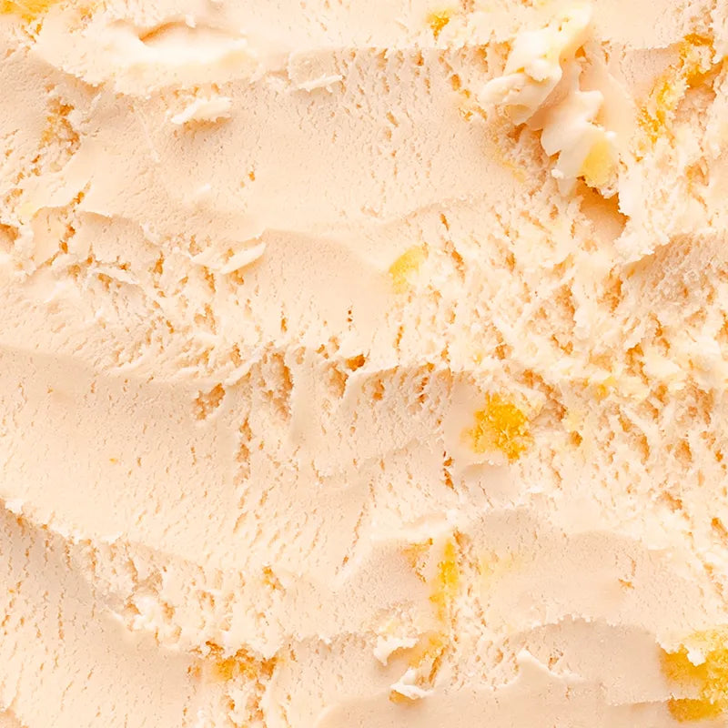 Peach ice cream close up: peachy orange ice cream with peach chunks peeking through. The picture is so close that it captures the individual chunks of peach and the ripples in the ice cream from scoops being taken out of it