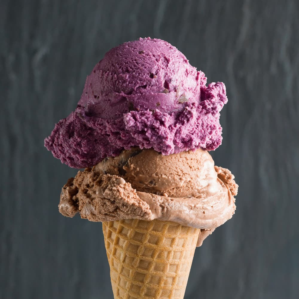 a perfect Double scoop cone with dark purple black raspberry chocolate chip and light brown dutch milk chocolate in front of a dark grey background