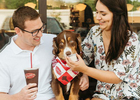 two happy people with their puppy in a bandana in between them eating a dogster's treat