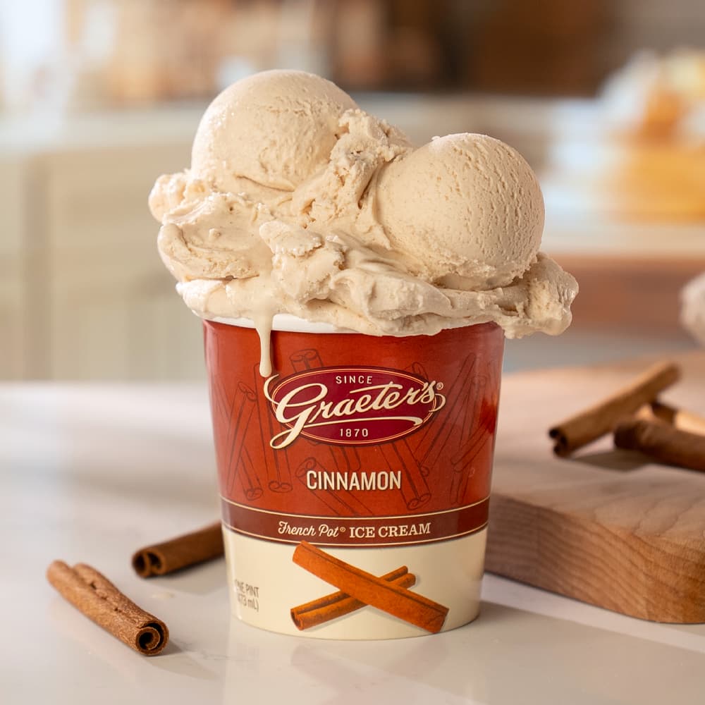 Graeter's cinnamon ice cream in a red pint with cinnamon sticks on a counter.