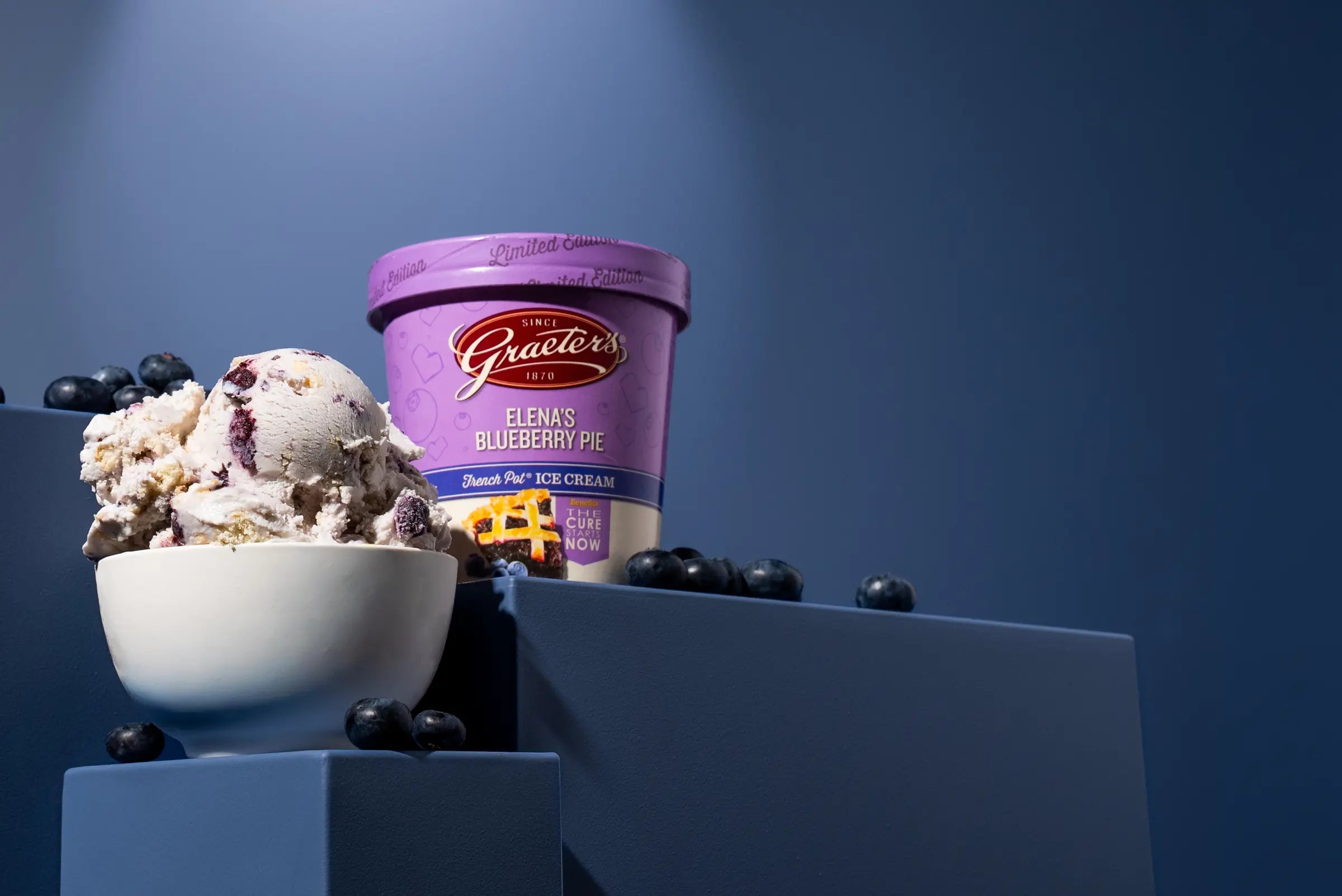 September fountain menu: Elena's blueberry pie ice cream, a light purple ice cream with blueberries and pie crust within, in a bowl next to the pint with blueberries scattered around