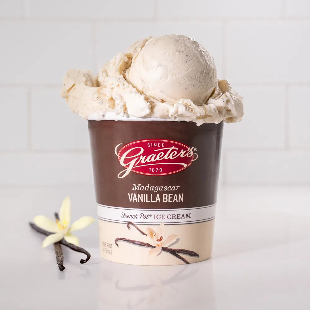 Graeter's Madagascar Vanilla Bean ice pint: cream ice cream with black vanilla speckles overflowing from a pint with a vanilla pod sitting next to it in front of a white background